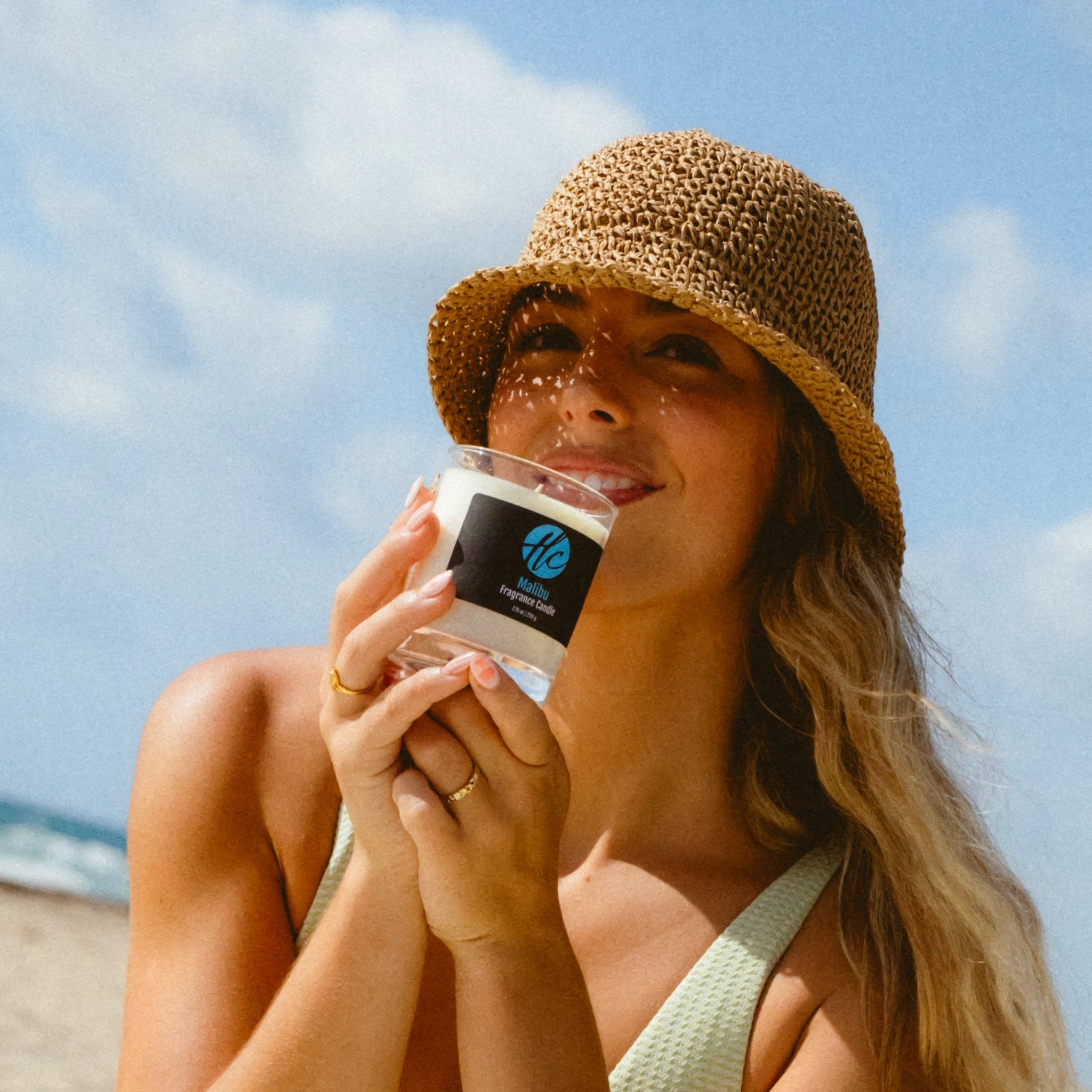 Woman holding Halcyon Coast Malibu non-toxic fragrance candle at the beach, inspired by sun, sand, and California vibes.
