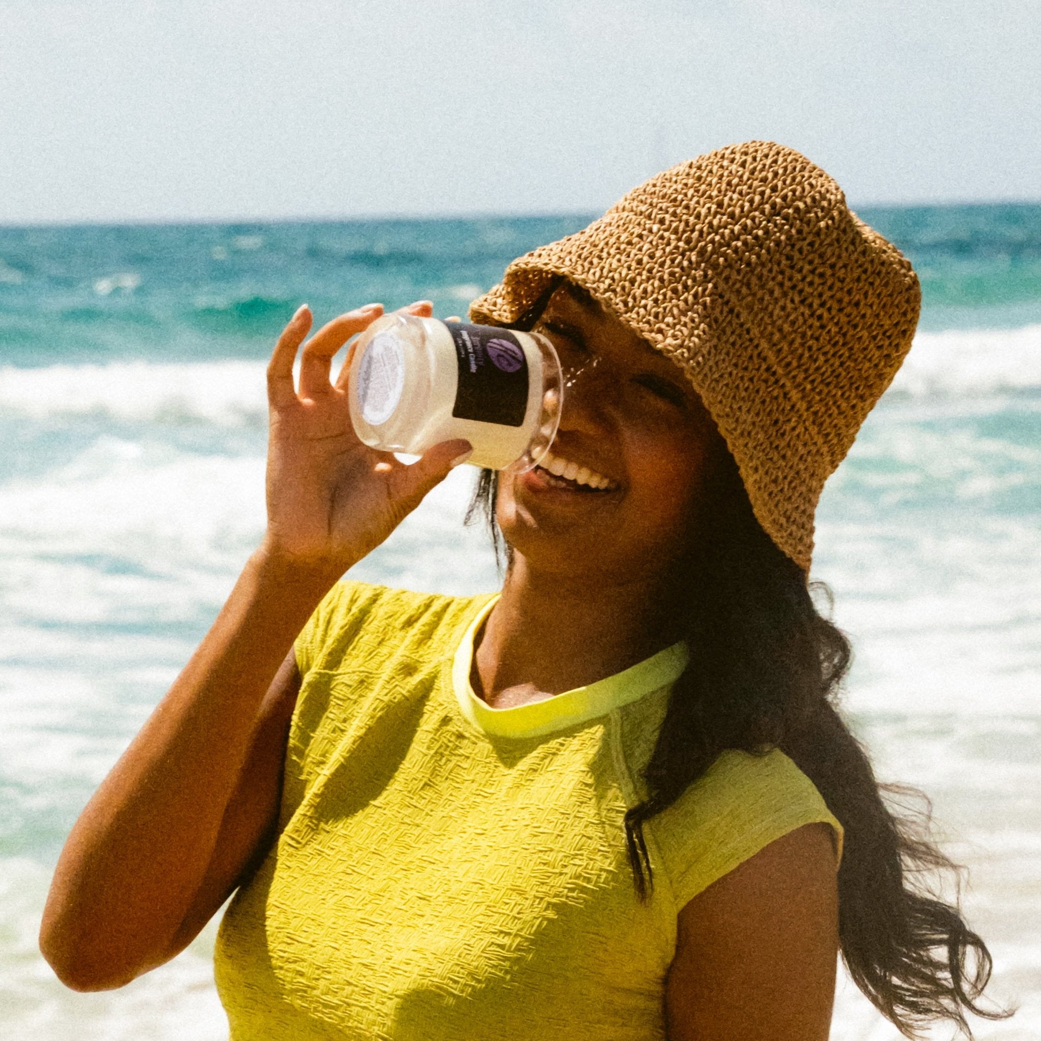 Smiling woman on the beach holding Halcyon Coast non-toxic fragrance candle, inspired by California’s coastal vibes.